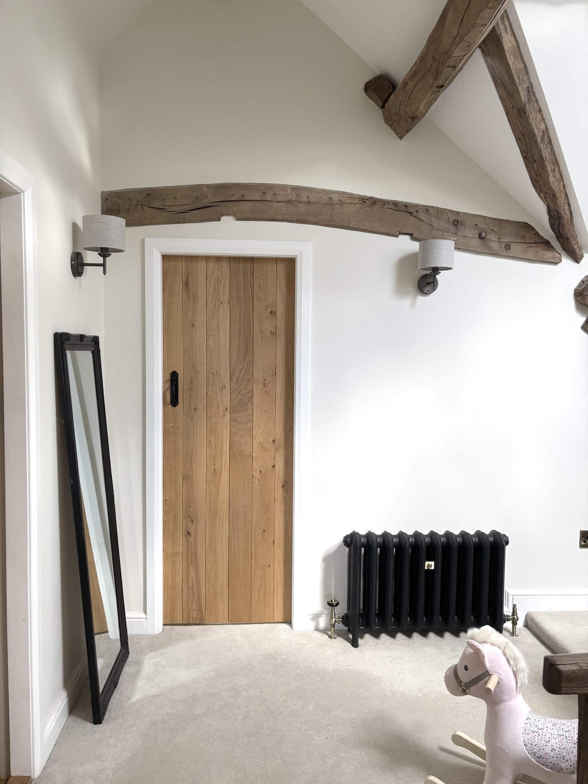 Stylish room with wooden beams, cast iron radiator and a mirror leaning against the wall. A child's rocking horse sits on the cream carpet.